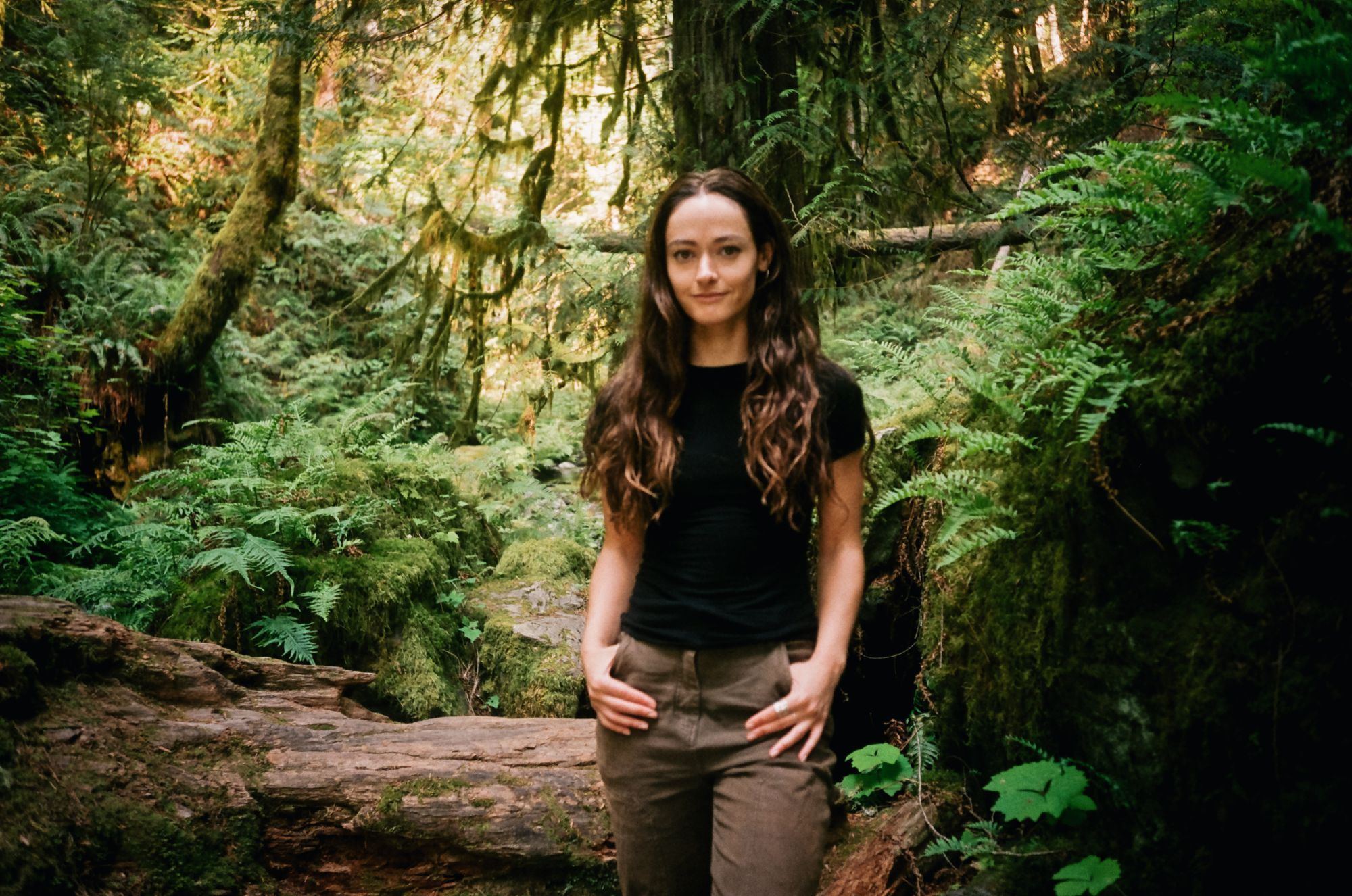 Maia Wikler standing among ferns and mossy logs in a coastal rainforest